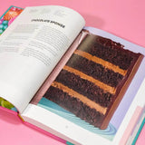 Open Crumbs & Doilies Recipe Book showing chocolate sponge cake recipe and full-color photo of layered cake slice.